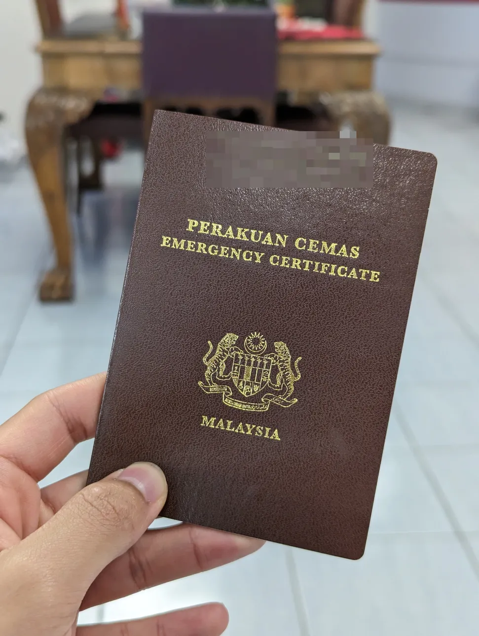 A picture of a Malaysian Emergency Certificate being held up by hand, issued in the year 2024 by the Malaysian Embassy in Bucharest, Romania